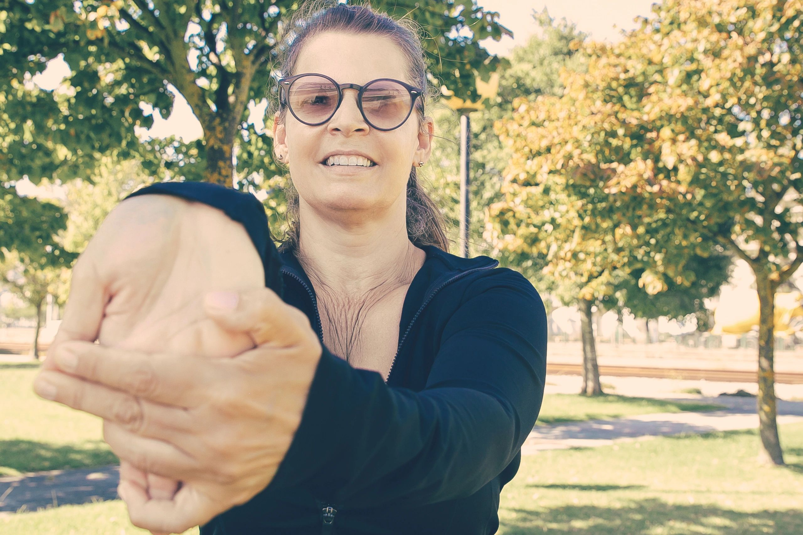 Middle-aged woman stretching her wrist and arm muscles outdoors as part of a warm-up.